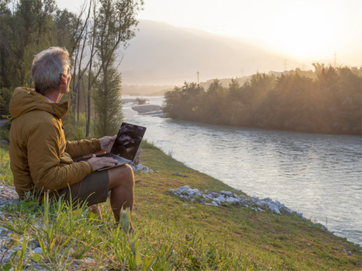 El hombre que trabaja en la computadora portátil se relaja cerca del río